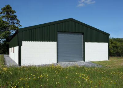 Newly constructed barn of cream painted concrete block walls with a green metal sheet roof and roller shutter doors, standing in a field of buttercups, with a blue sky and trees to the rear.